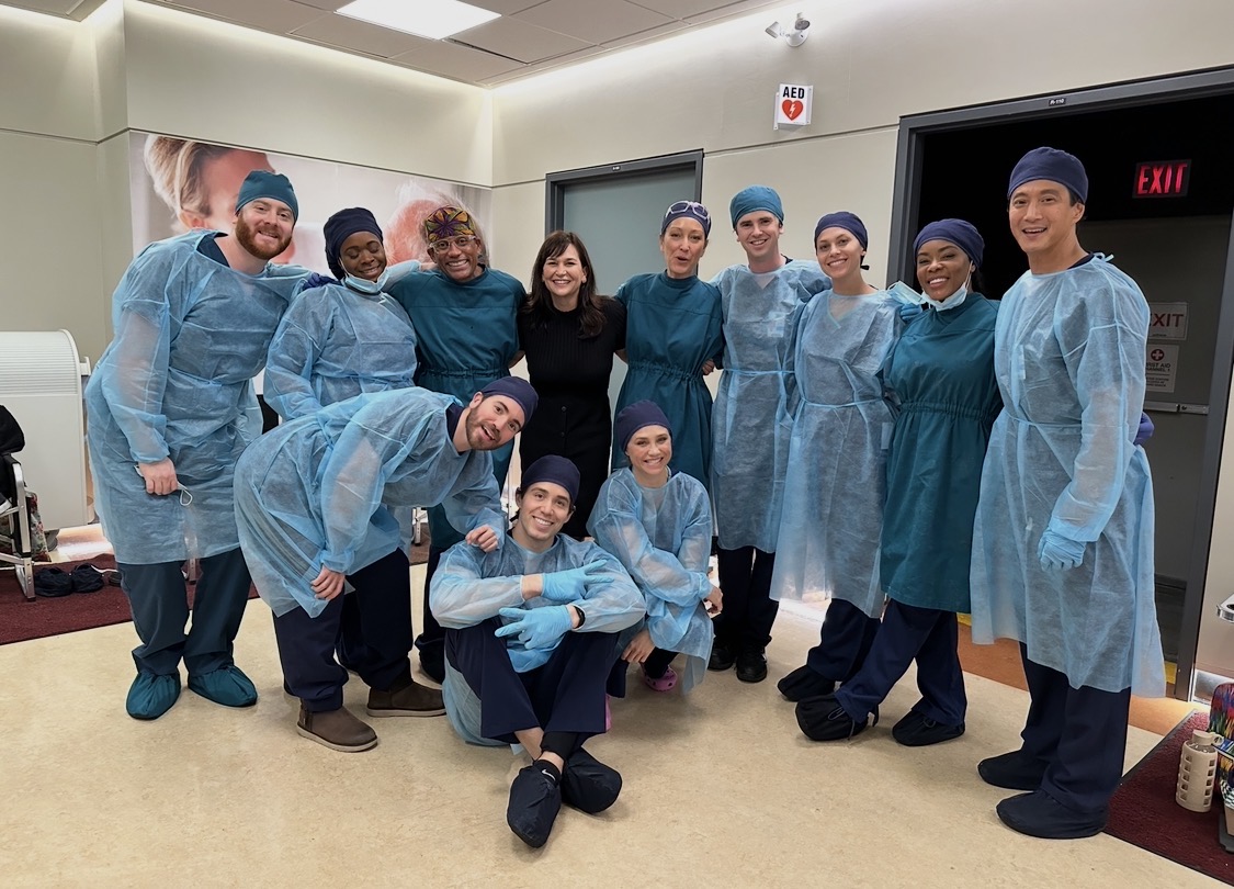 A group gathered in a medical setting, with several people wearing surgical gowns.