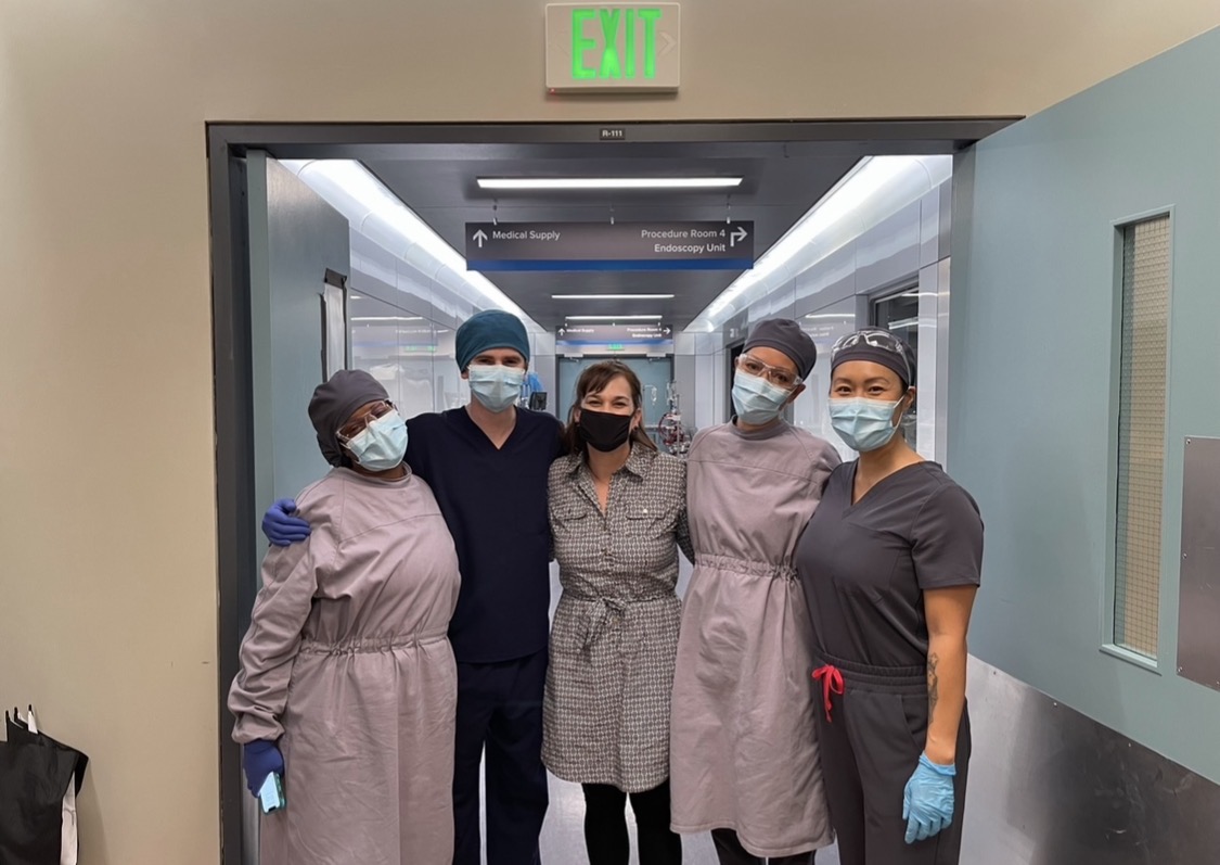 A group photographed together in a medical corridor, with several people in surgical clothing.